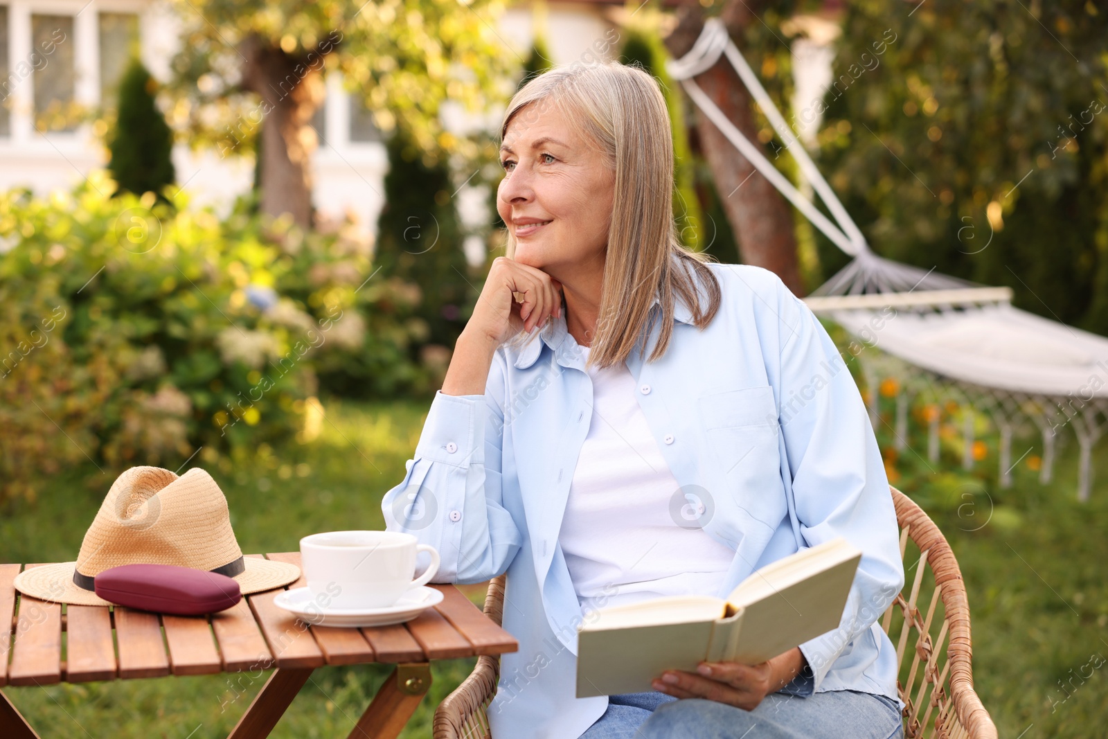 Photo of Senior woman reading book at wooden table in garden