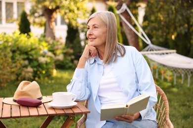 Photo of Senior woman reading book at wooden table in garden