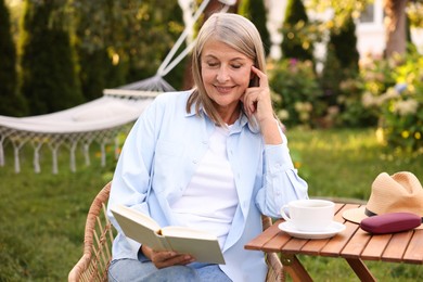 Photo of Senior woman reading book at wooden table in garden