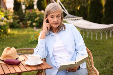 Photo of Senior woman reading book at wooden table in garden