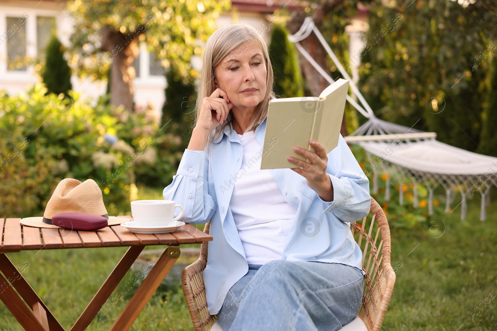 Photo of Senior woman reading book at wooden table in garden