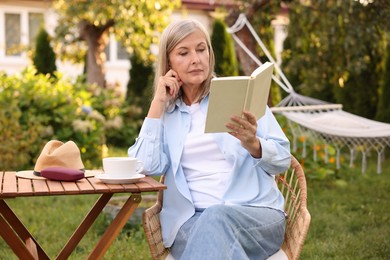 Photo of Senior woman reading book at wooden table in garden