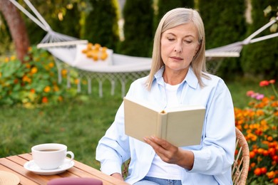 Photo of Senior woman reading book at wooden table in garden