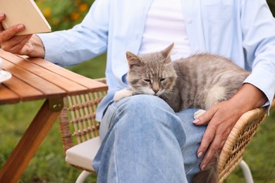 Photo of Senior woman with cat reading book at wooden table in garden, closeup