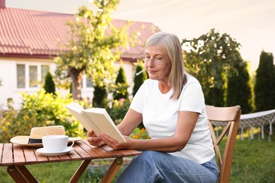 Photo of Senior woman reading book at wooden table in garden