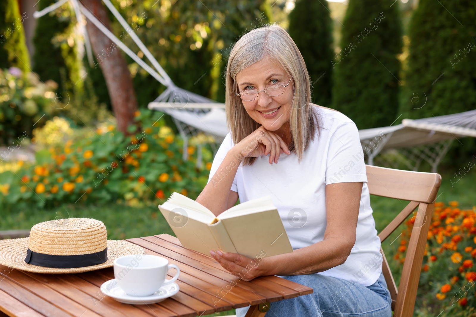 Photo of Senior woman reading book at wooden table in garden