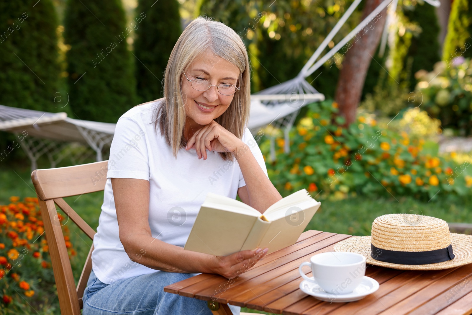 Photo of Senior woman reading book at wooden table in garden