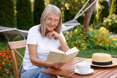 Photo of Senior woman reading book at wooden table in garden