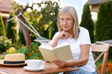 Photo of Senior woman reading book at wooden table in garden