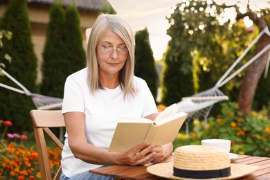Photo of Senior woman reading book at wooden table in garden