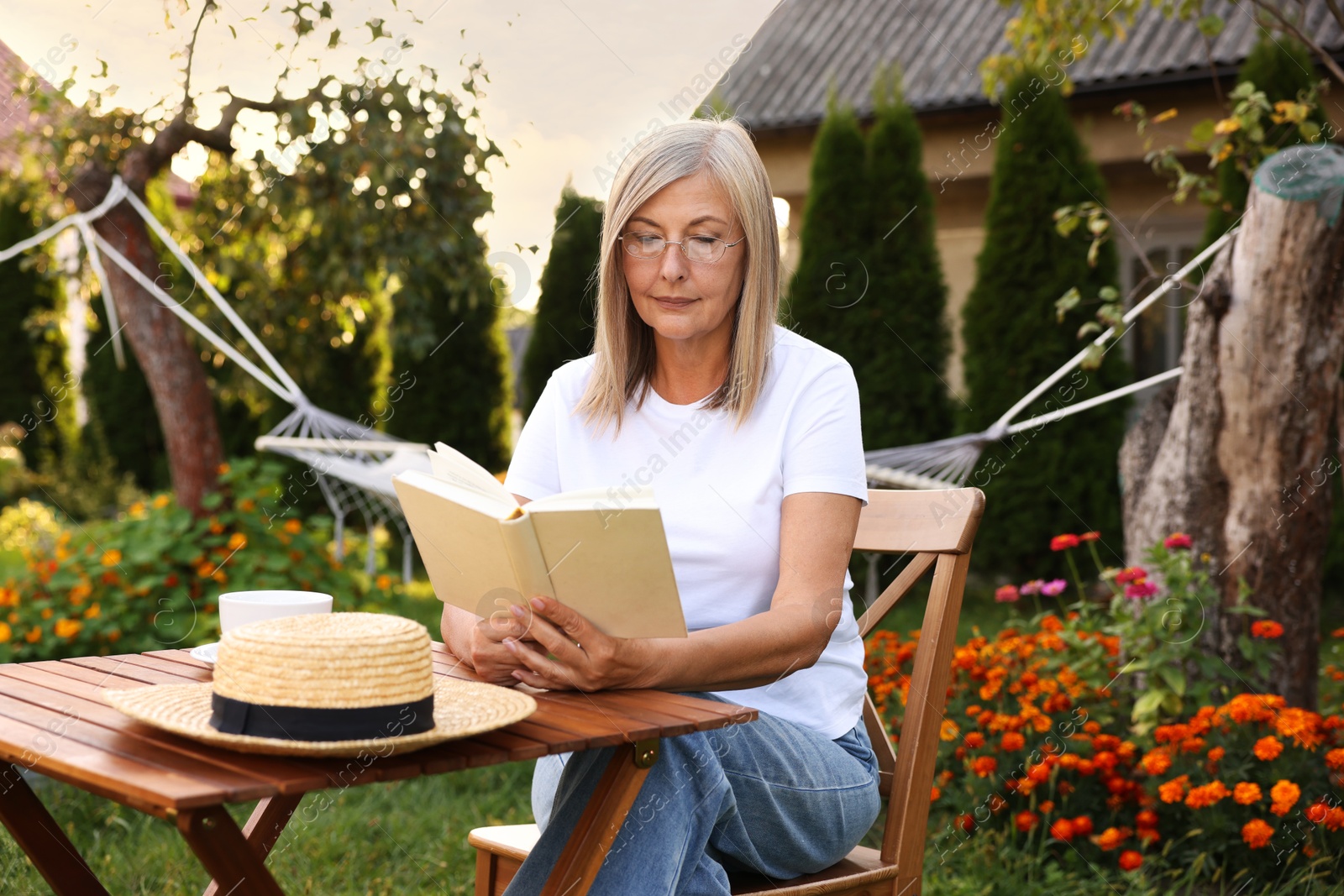 Photo of Senior woman reading book at wooden table in garden