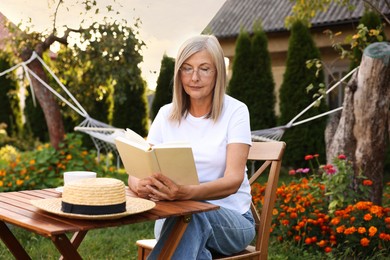 Photo of Senior woman reading book at wooden table in garden