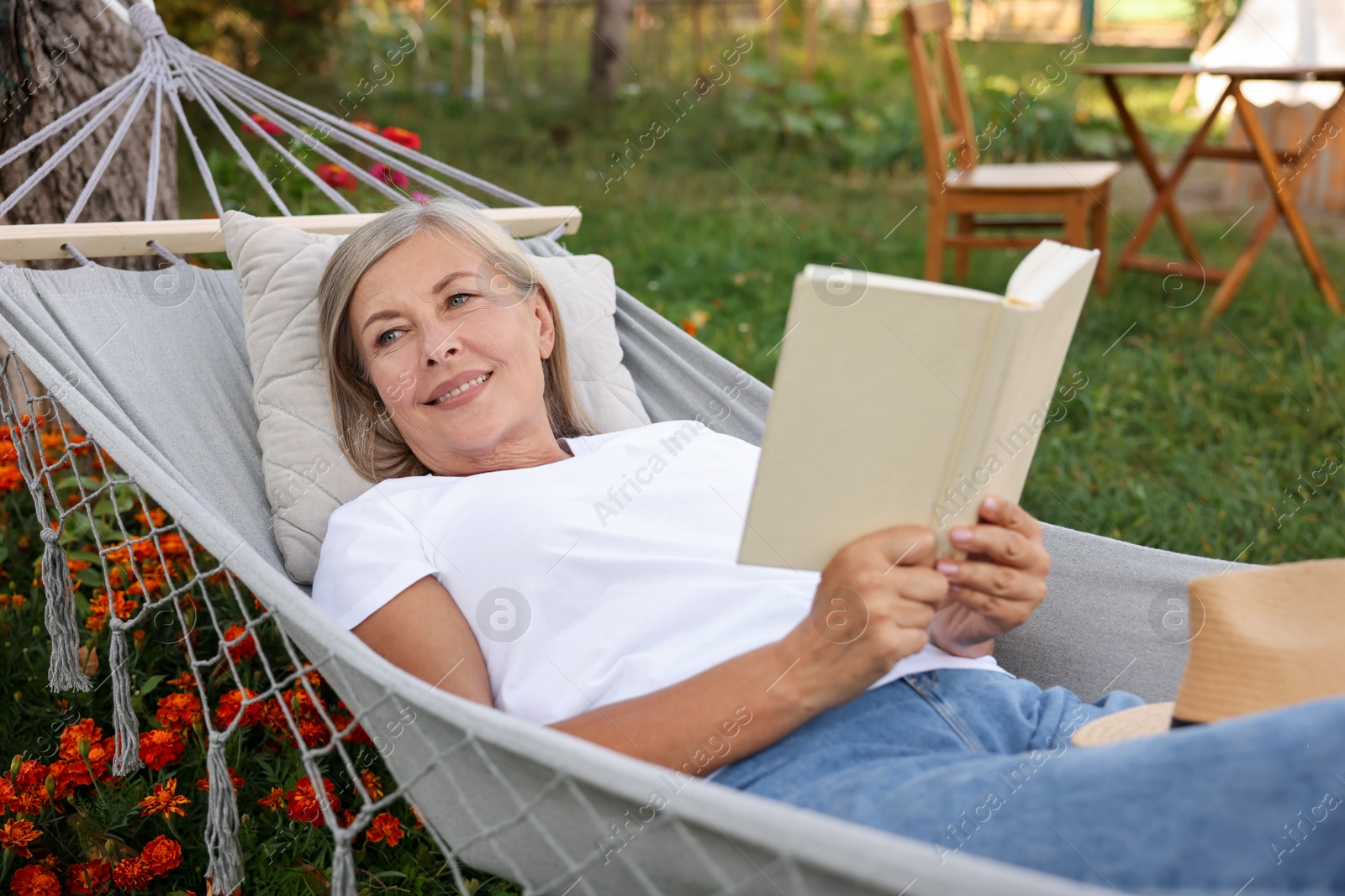 Photo of Senior woman with book resting in hammock outdoors