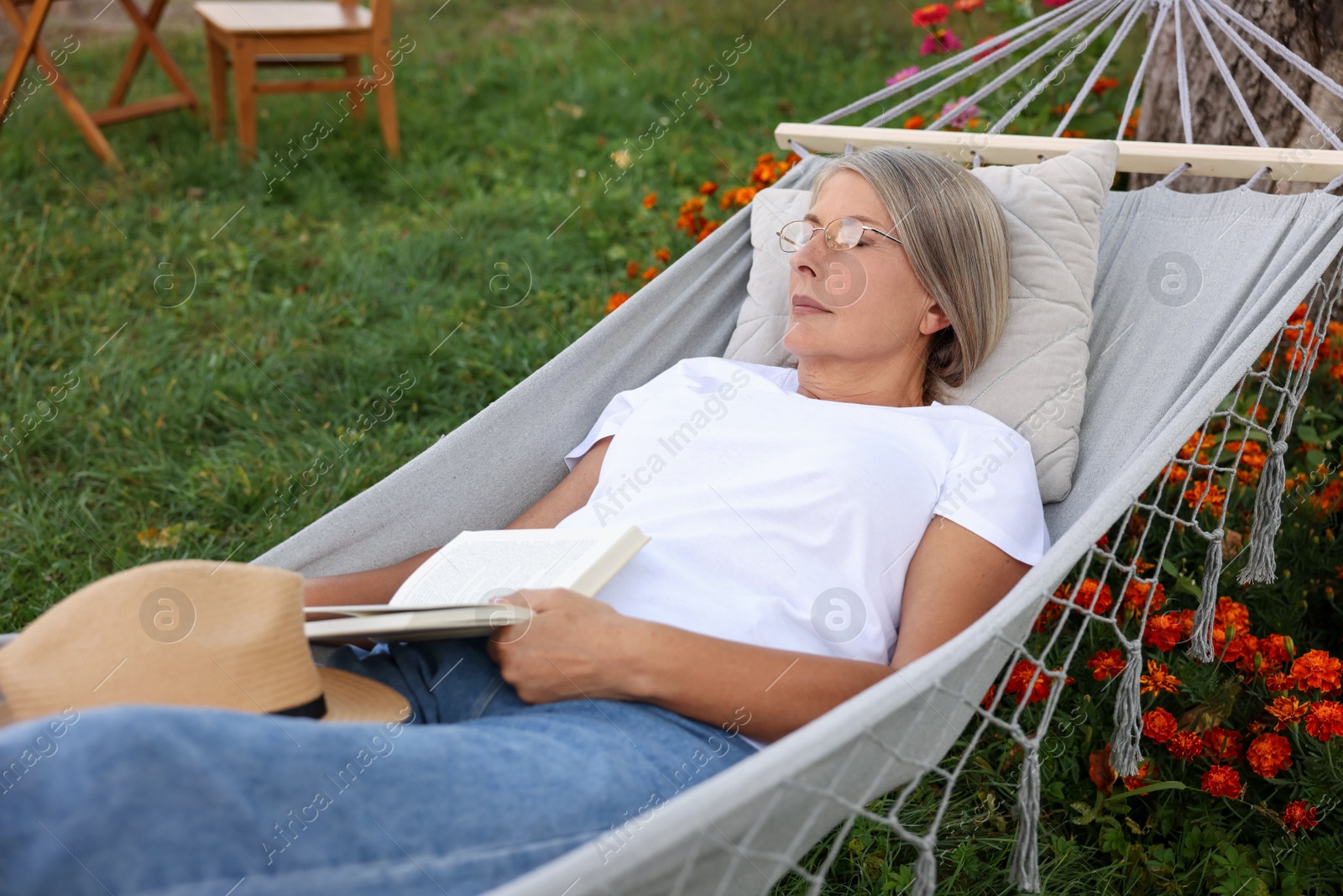Photo of Senior woman with book resting in hammock outdoors