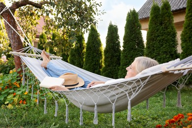Photo of Senior woman with book resting in hammock outdoors