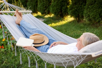 Photo of Senior woman with book resting in hammock outdoors
