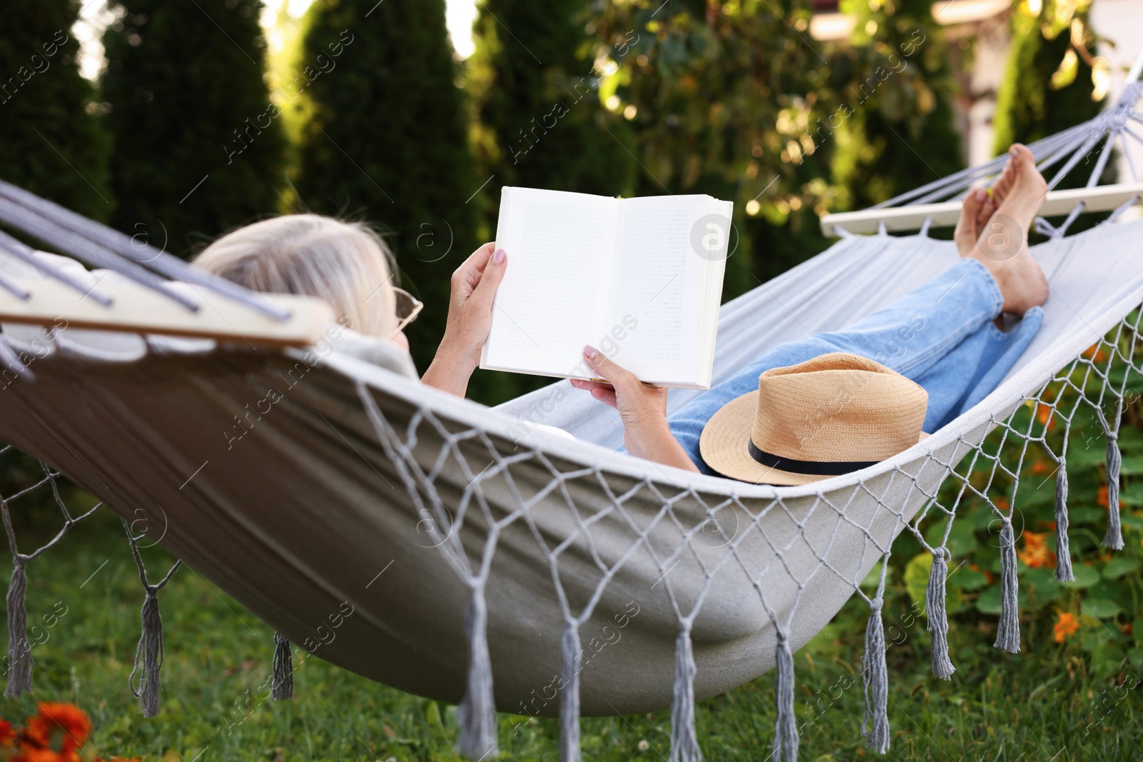 Photo of Senior woman reading book in comfortable hammock outdoors