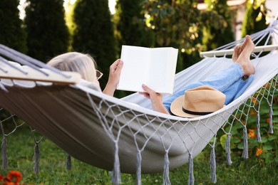 Photo of Senior woman reading book in comfortable hammock outdoors