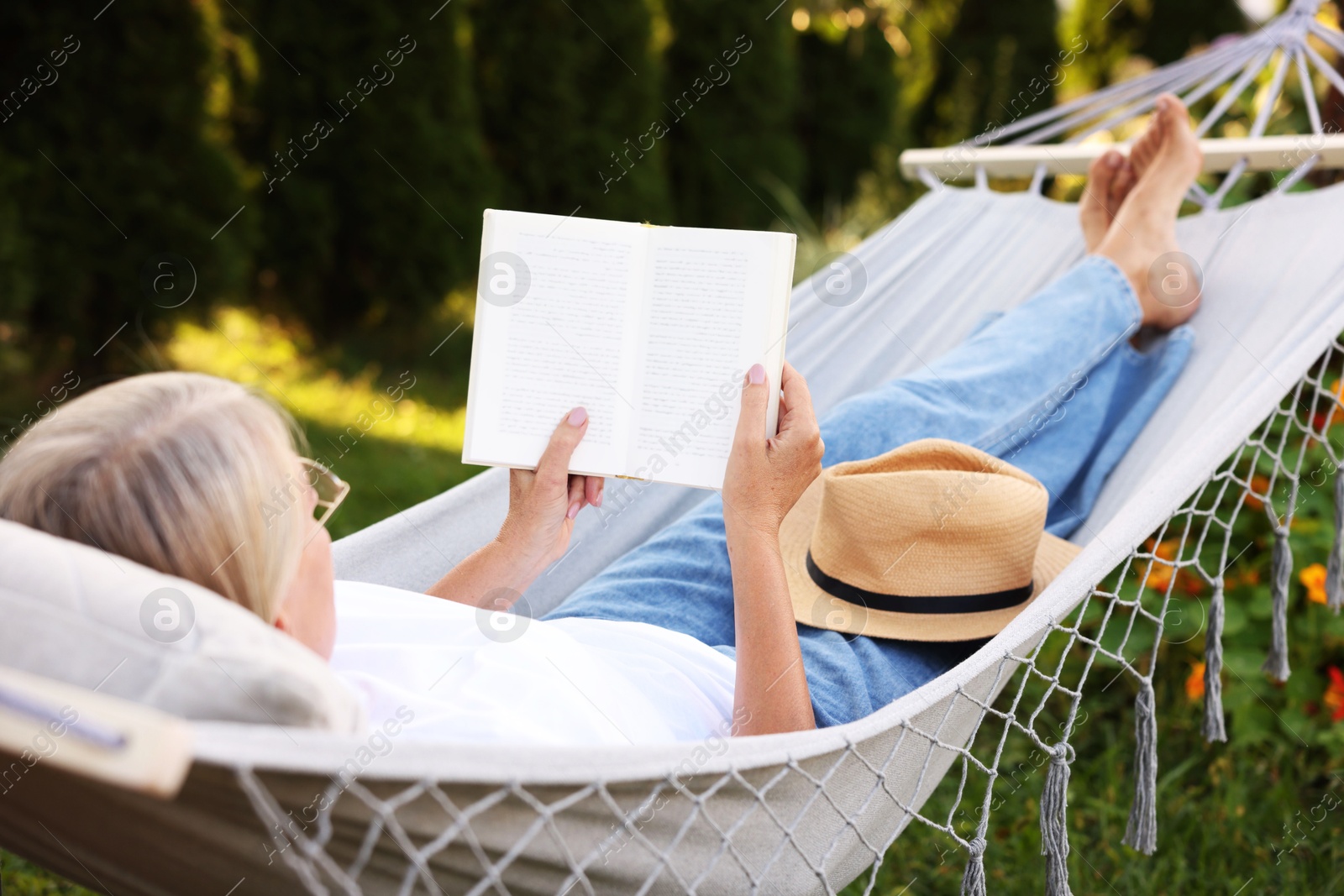 Photo of Senior woman reading book in hammock outdoors