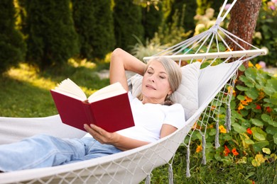 Photo of Senior woman reading book in hammock outdoors