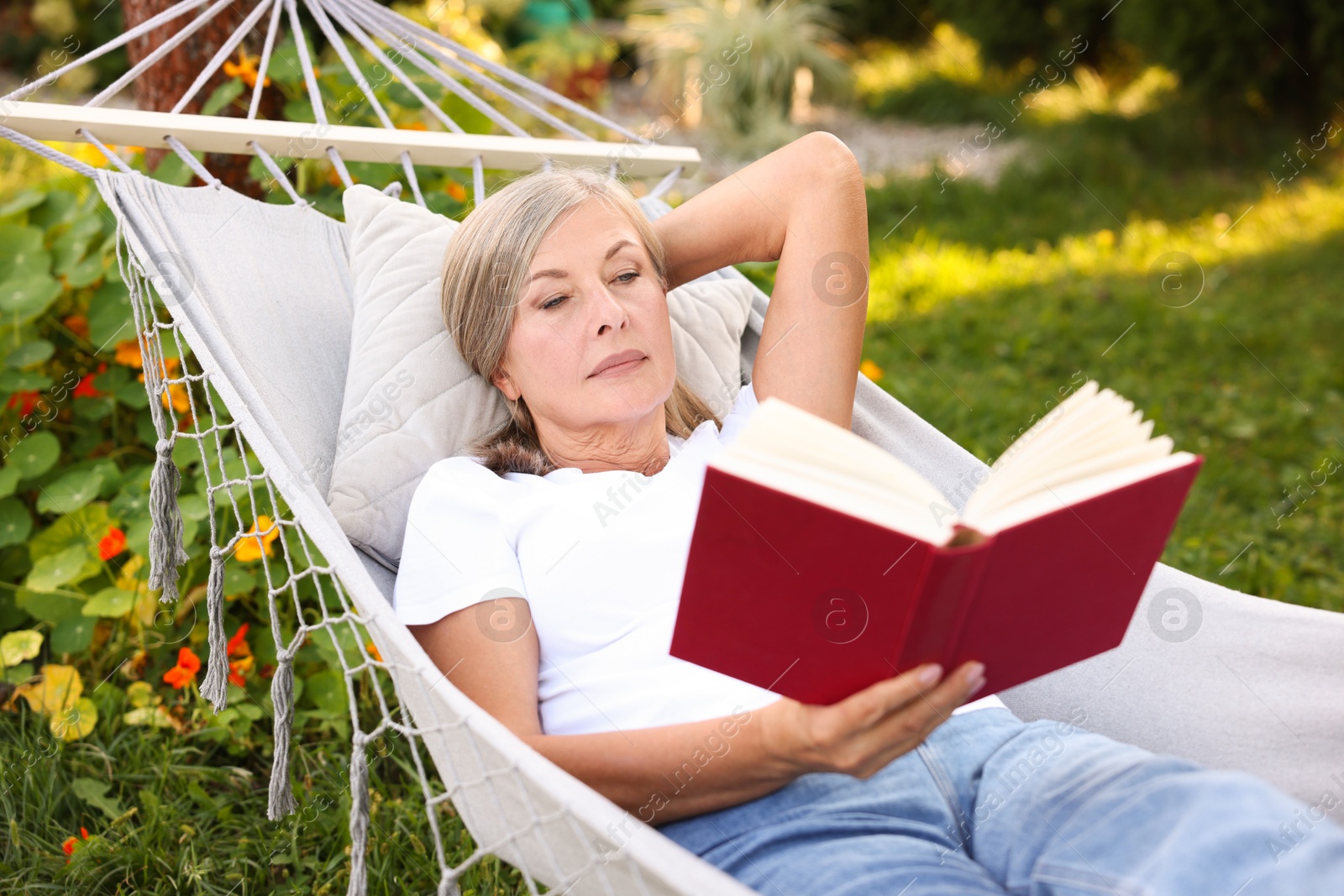 Photo of Senior woman reading book in hammock outdoors