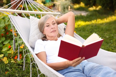 Photo of Senior woman reading book in hammock outdoors
