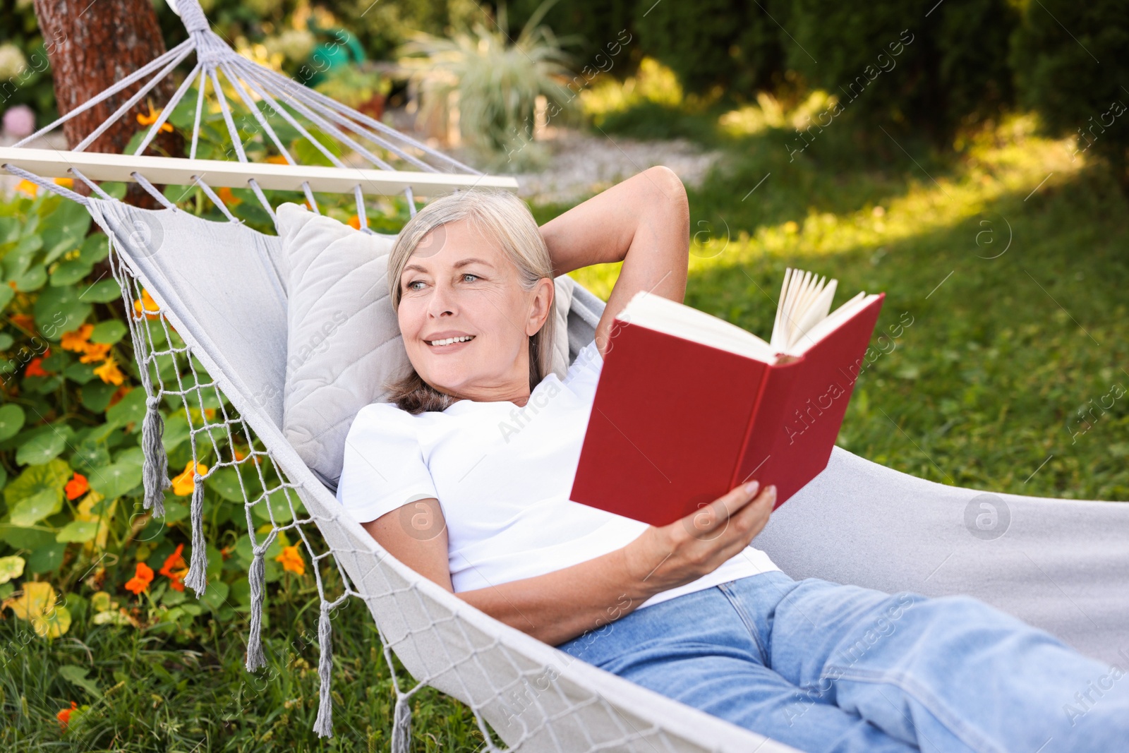 Photo of Senior woman with book resting in hammock outdoors