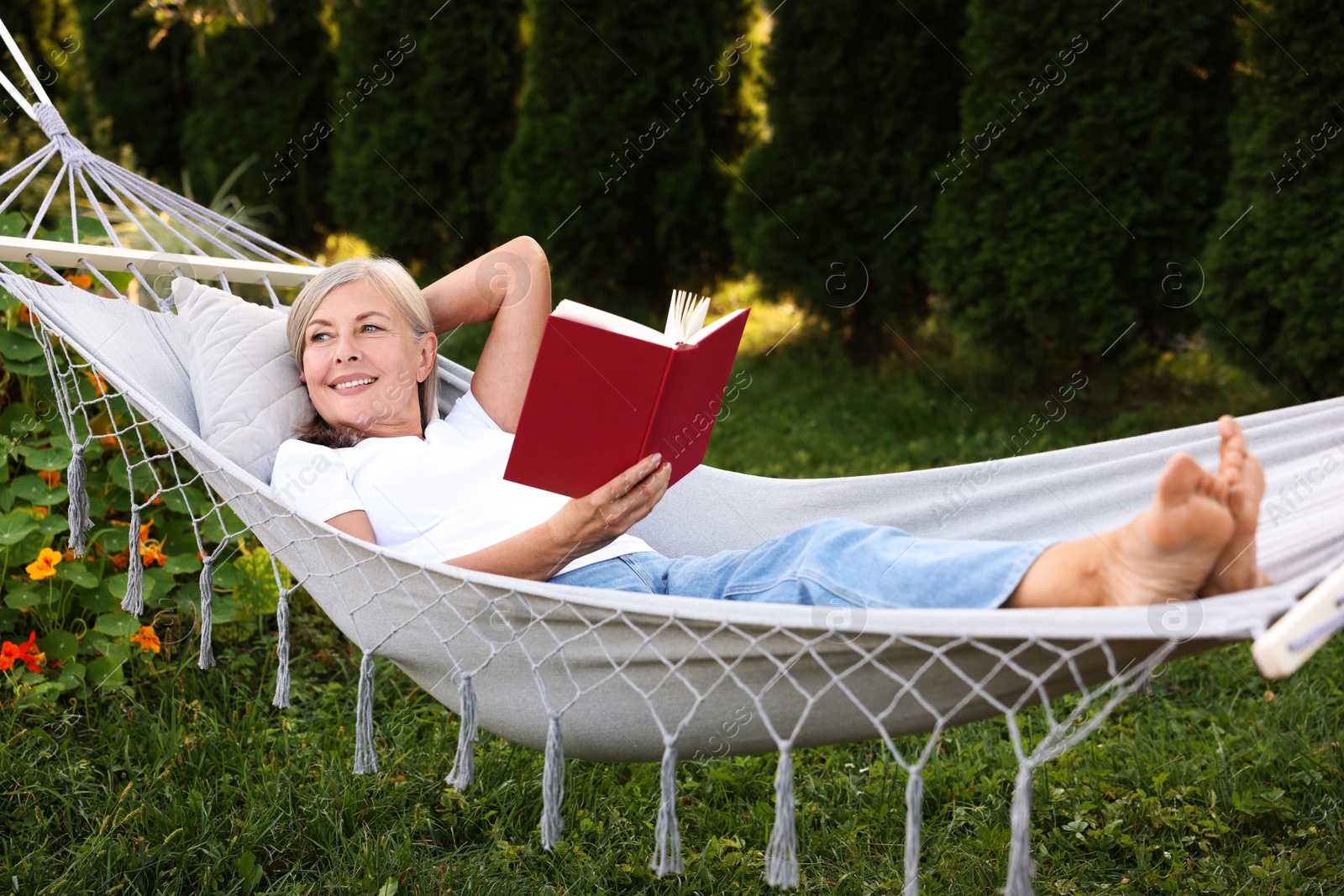 Photo of Senior woman with book resting in hammock outdoors