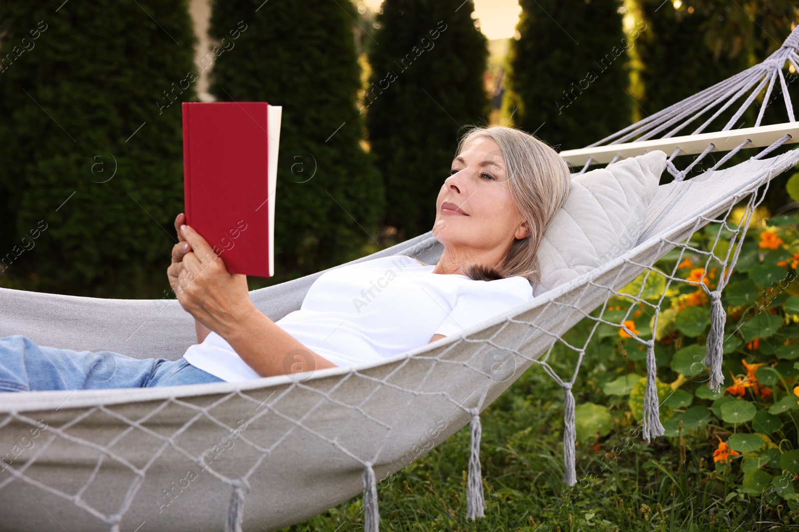 Photo of Senior woman reading book in hammock outdoors