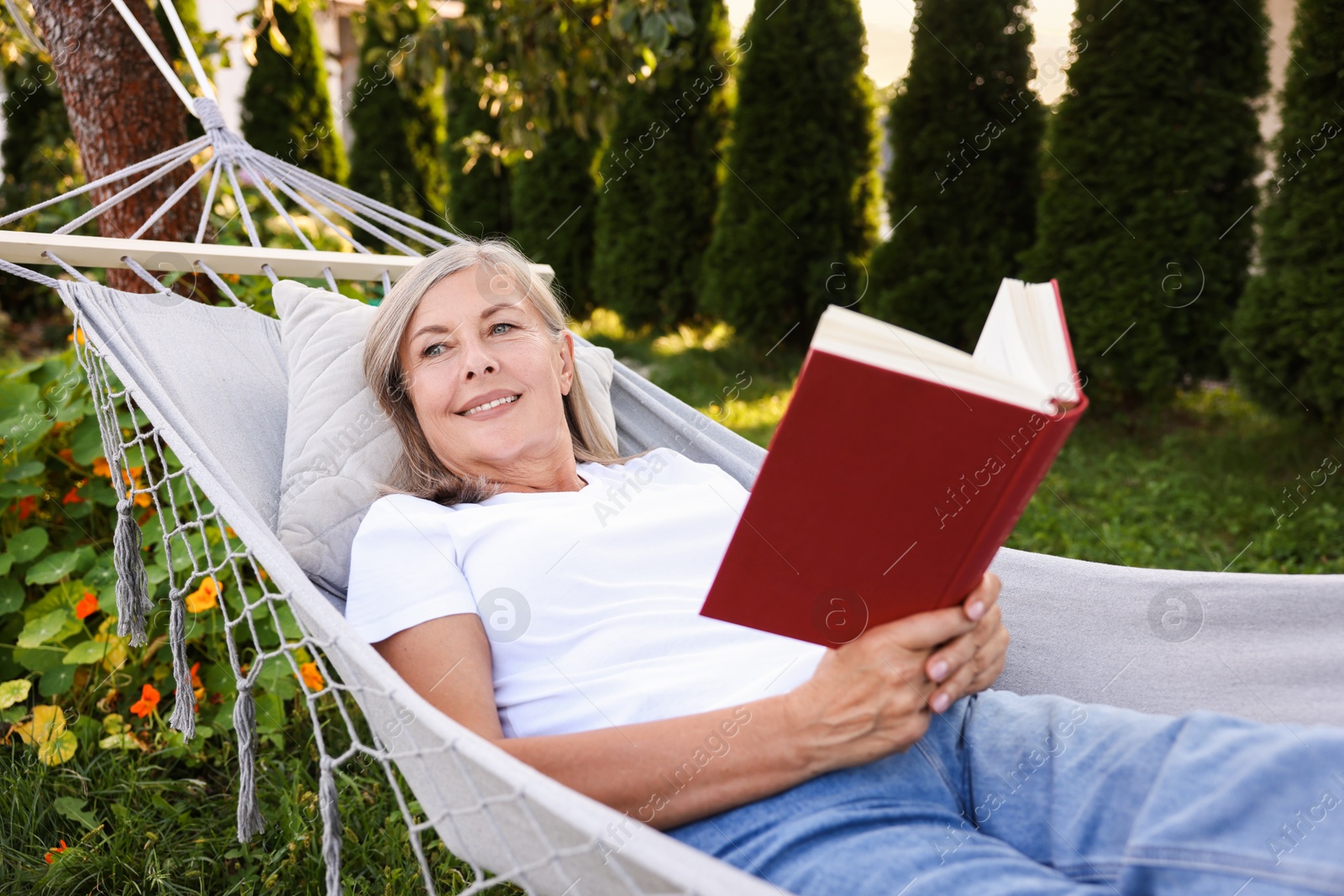 Photo of Senior woman with book resting in hammock outdoors