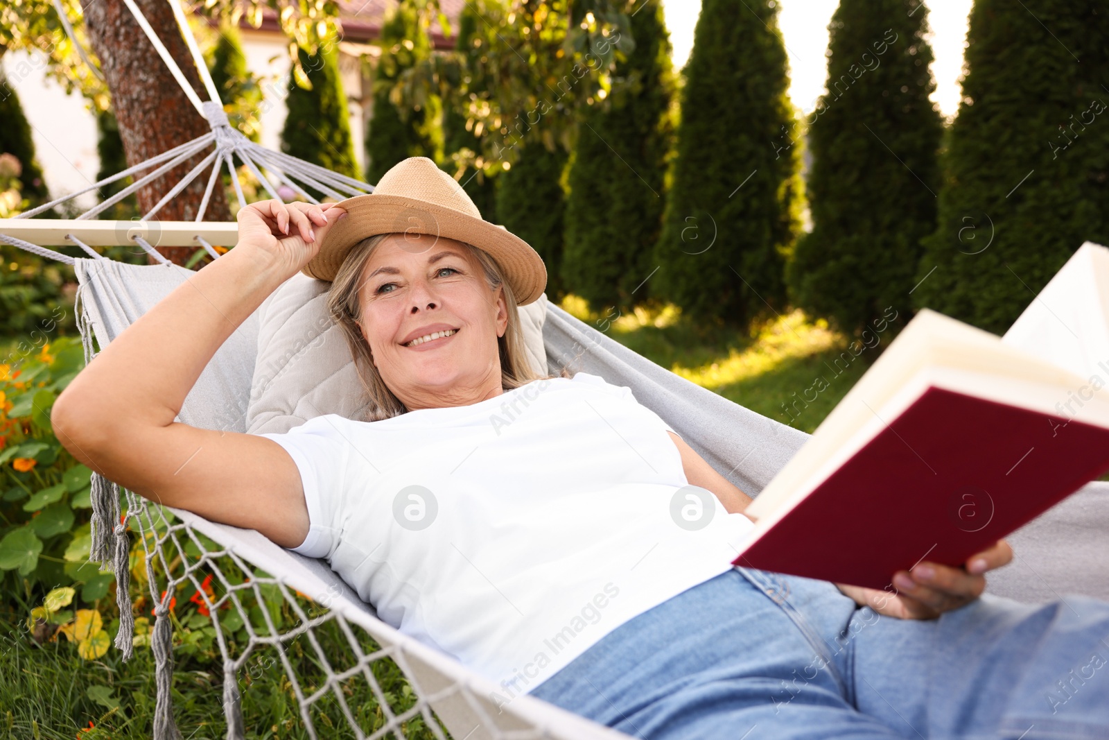 Photo of Senior woman with book resting in hammock outdoors