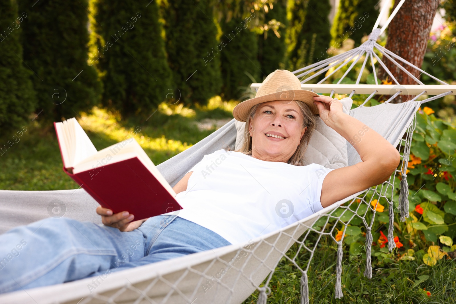 Photo of Senior woman with book resting in hammock outdoors