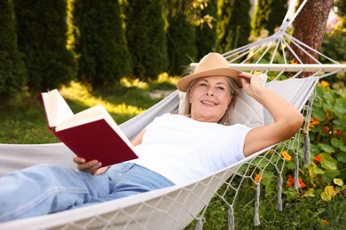 Photo of Senior woman with book resting in hammock outdoors