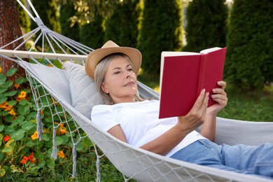 Photo of Senior woman reading book in hammock outdoors