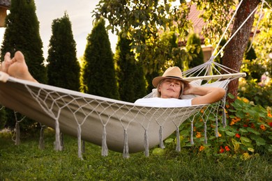 Photo of Senior woman in straw hat resting in hammock outdoors