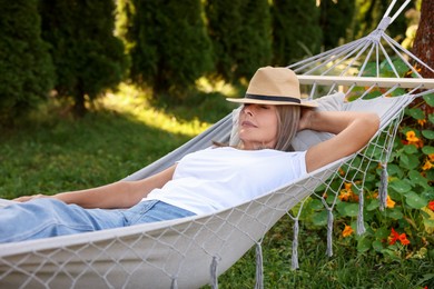 Photo of Senior woman in straw hat resting in hammock outdoors