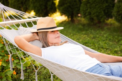 Photo of Senior woman in straw hat resting in hammock outdoors