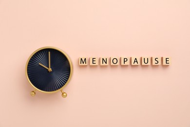 Photo of Wooden cubes with word Menopause and alarm clock on beige background, top view