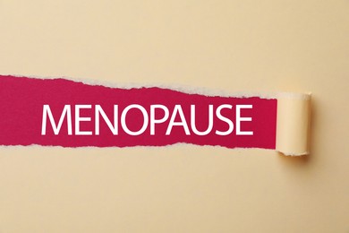 Photo of Word Menopause on crimson background, view through hole in torn beige paper