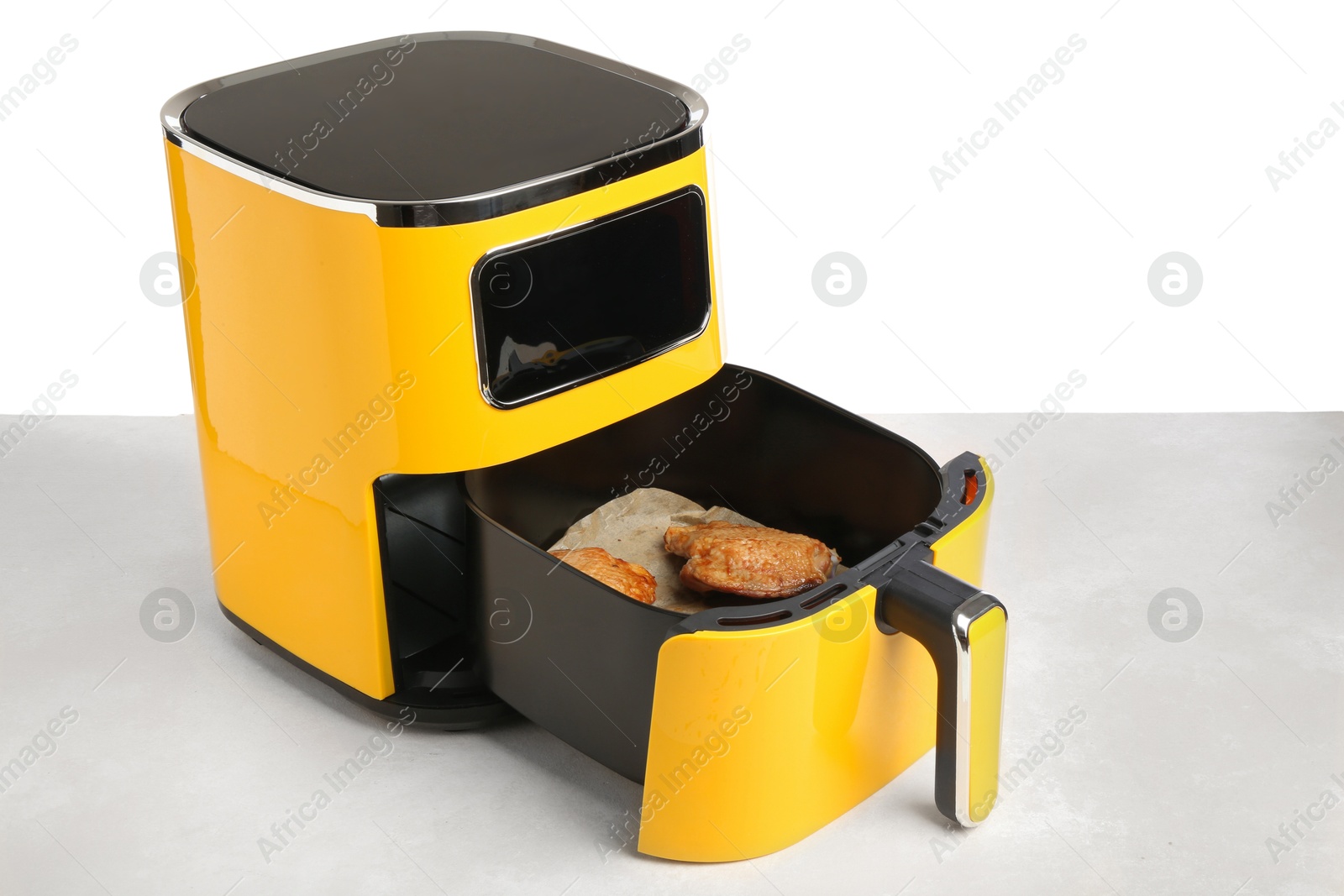 Photo of Air fryer with cooked chicken thighs on table against white background