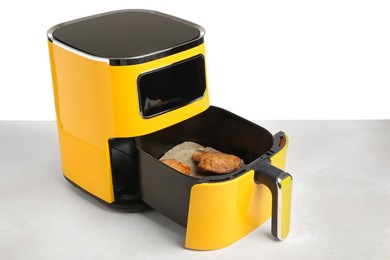 Photo of Air fryer with cooked chicken thighs on table against white background