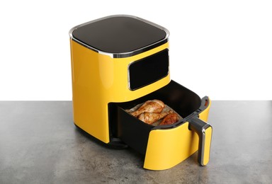 Photo of Air fryer with cooked chicken drumsticks on grey table against white background