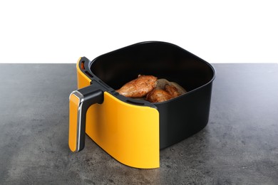 Photo of Air fryer basket with chicken drumsticks on grey table against white background