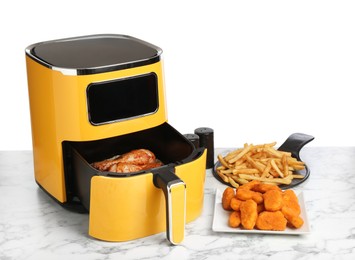 Photo of Modern air fryer and cooked meals on marble table against white background