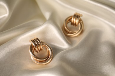 Photo of Stylish gold earrings on light silk cloth, closeup