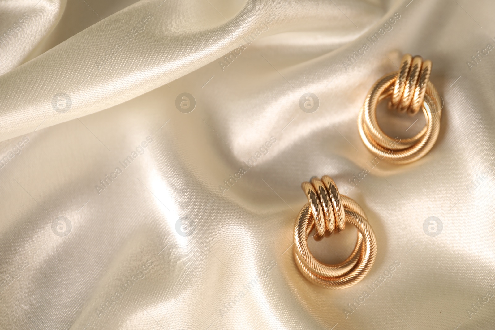 Photo of Stylish gold earrings on light silk cloth, top view. Space for text