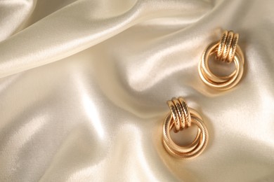Photo of Stylish gold earrings on light silk cloth, top view. Space for text