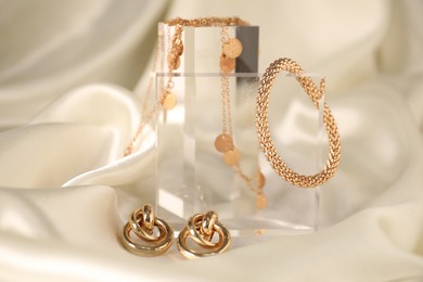 Photo of Stylish presentation of gold jewelry on light silk cloth, closeup