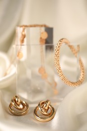 Photo of Stylish presentation of gold jewelry on light silk cloth, closeup