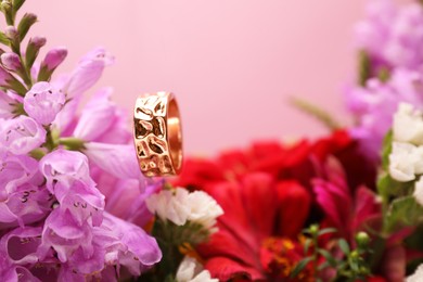 Photo of Stylish gold ring and beautiful flowers against pink background, closeup